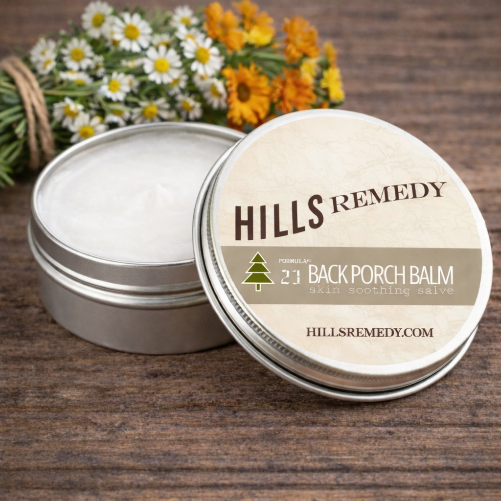 Hills Remedy Back Porch Balm tin on a wooden surface with flowers in the background