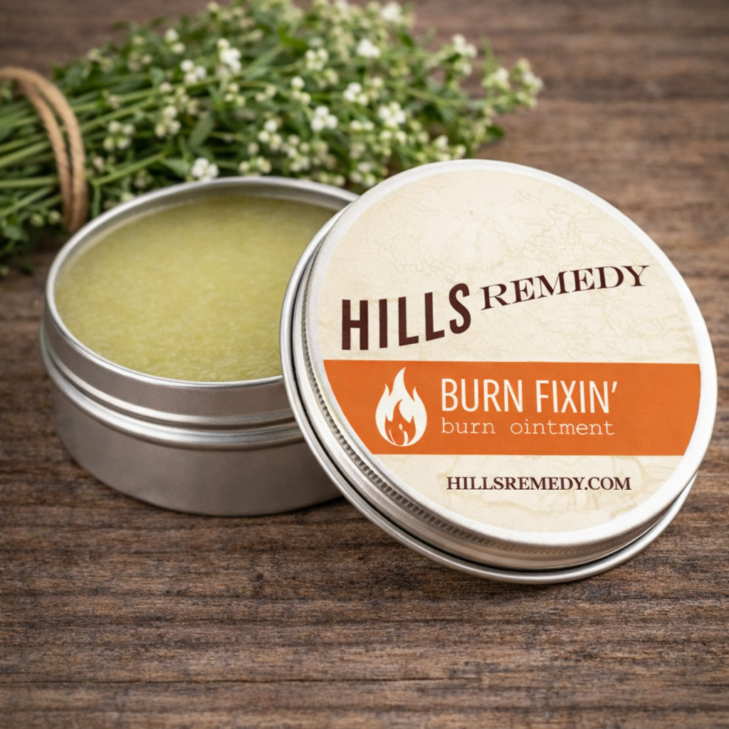 Hills Remedy burn ointment tin on a wooden surface with herbs in the background