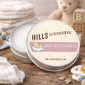 Hills Remedy Baby Bottom Balm tin on a wooden surface with toys in the background