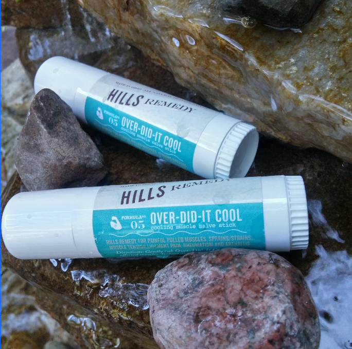 Two 'Hills Remedy' overdid-it cool muscle salve sticks on rocks by a water source.